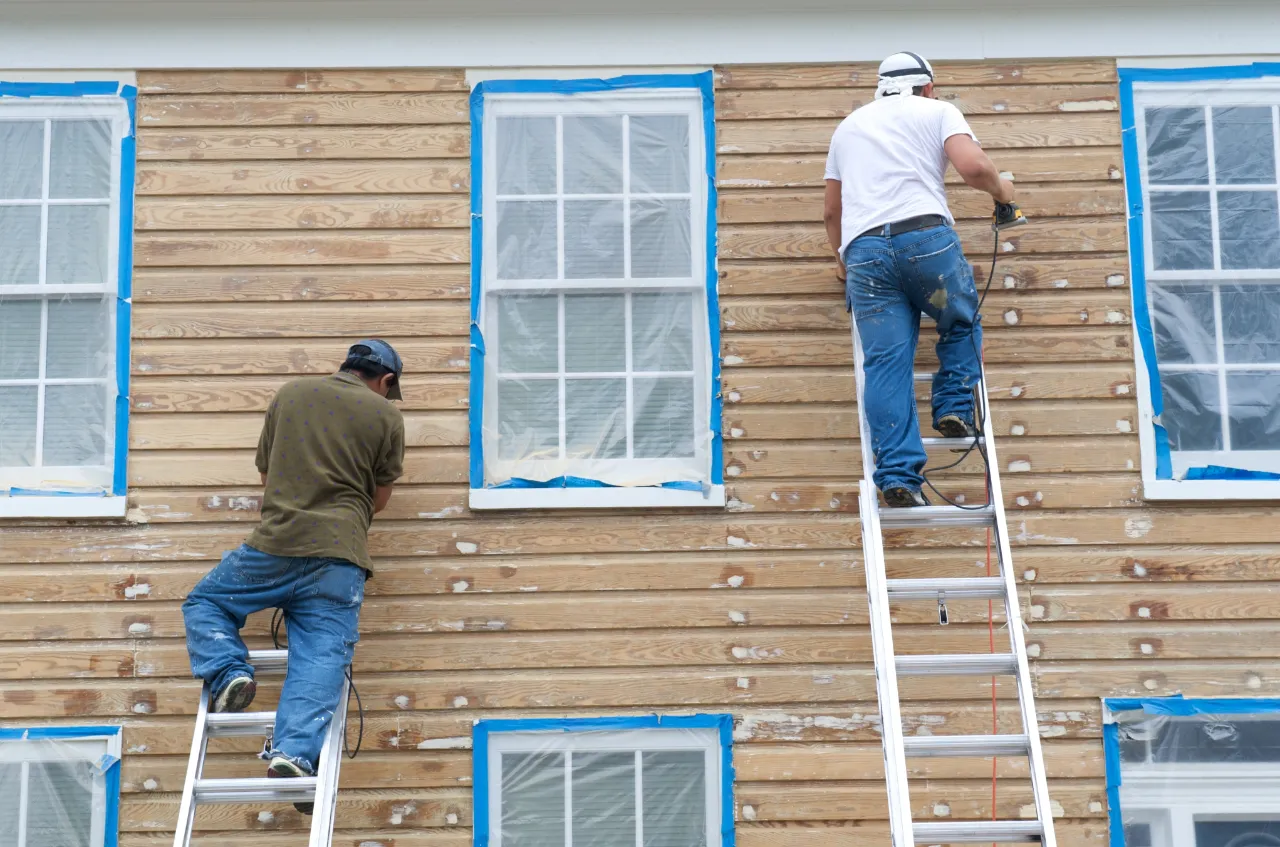 Two men working on house siding with ladders in New Jersey